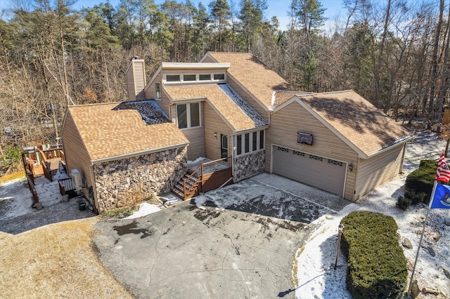 view of front facade with driveway, stone siding, a chimney, roof with shingles, and an attached garage