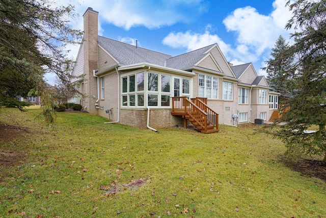 back of property with brick siding, a chimney, a lawn, central AC unit, and a sunroom