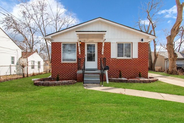 bungalow featuring brick siding, board and batten siding, a front lawn, and fence