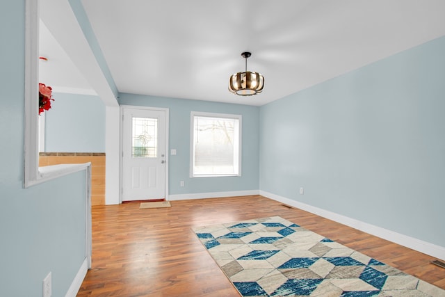 foyer entrance featuring a chandelier, baseboards, visible vents, and wood finished floors