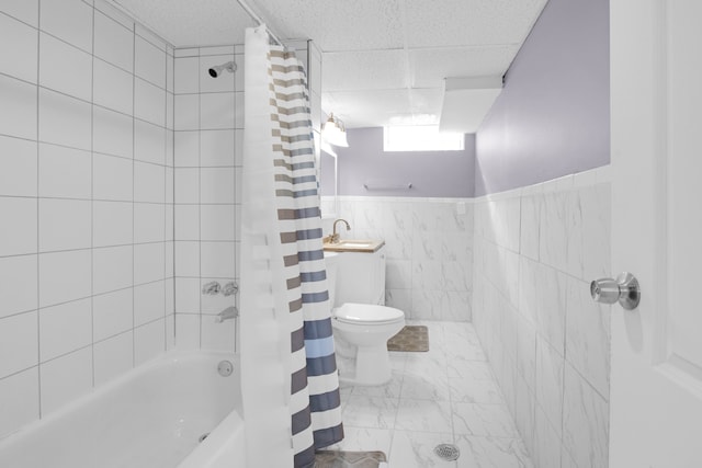 bathroom with a wainscoted wall, a drop ceiling, toilet, shower / bath combination with curtain, and tile walls