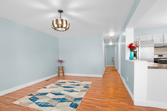 corridor featuring light wood-style flooring, an inviting chandelier, and baseboards