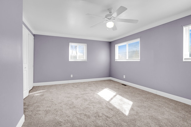 empty room featuring plenty of natural light, carpet flooring, baseboards, and a ceiling fan