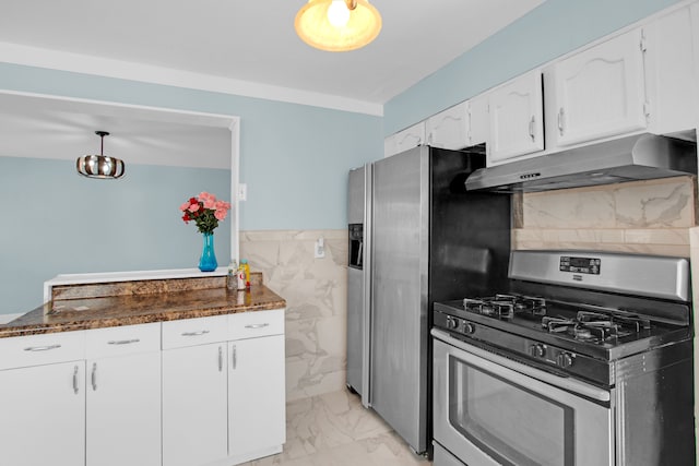 kitchen with under cabinet range hood, a wainscoted wall, stainless steel appliances, marble finish floor, and white cabinetry