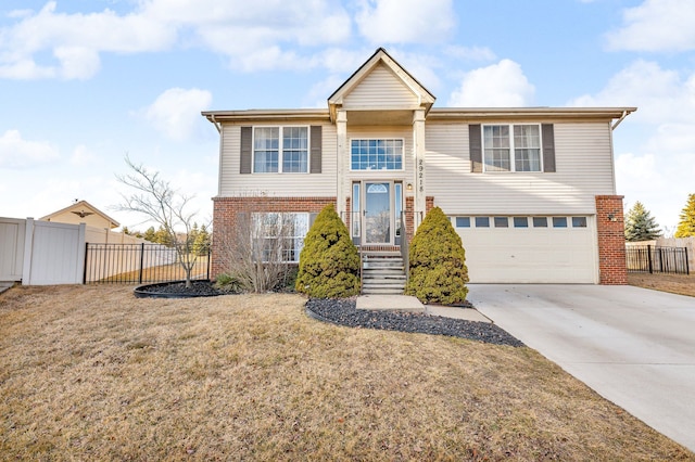 raised ranch featuring driveway, a garage, brick siding, fence, and a front yard