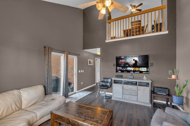 living area featuring a towering ceiling, dark wood-style floors, baseboards, and a ceiling fan