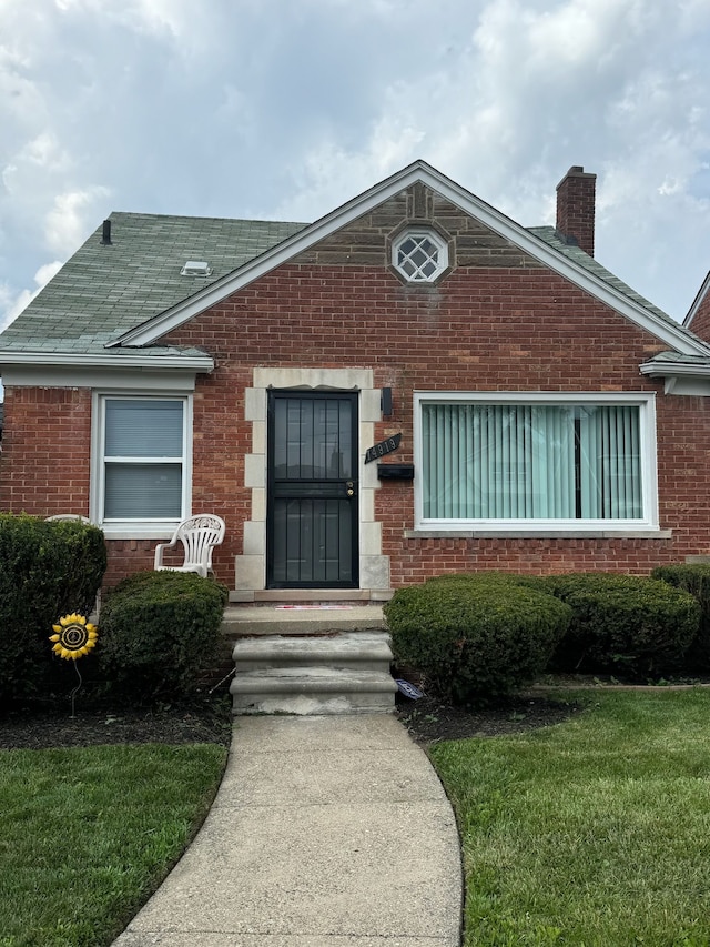 view of front of home with brick siding, a chimney, and roof with shingles