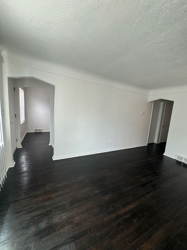 unfurnished room with dark wood-type flooring, arched walkways, visible vents, and baseboards