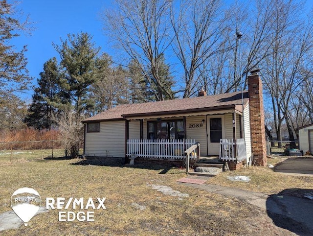 ranch-style home featuring roof with shingles, a chimney, a porch, fence, and a front lawn