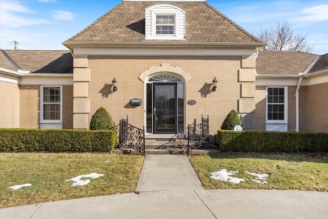 entrance to property with a yard, brick siding, and roof with shingles