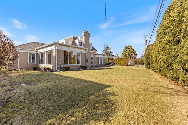 rear view of property featuring a yard, brick siding, and a chimney