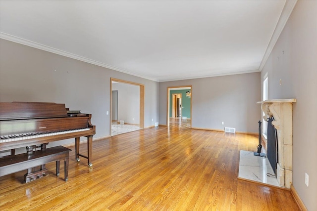 living area with baseboards, visible vents, ornamental molding, light wood-style floors, and a high end fireplace