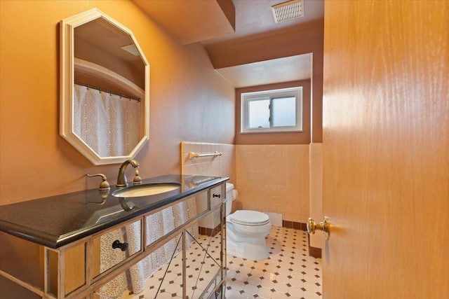 bathroom with visible vents, wainscoting, toilet, vanity, and tile walls