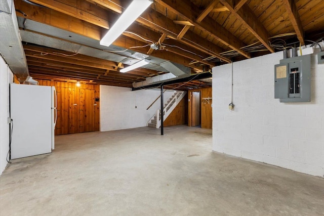 unfinished basement featuring stairs, freestanding refrigerator, and electric panel