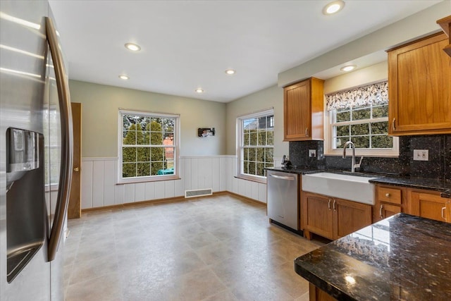 kitchen with visible vents, appliances with stainless steel finishes, brown cabinetry, wainscoting, and a sink