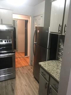 30200 Southfield Rd Unit 204, Southfield, MI 48076 - kitchen featuring appliances with stainless steel finishes, under cabinet range hood, light wood-style flooring, light stone countertops, and white cabinets
