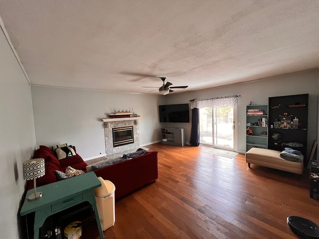 living area featuring a textured ceiling, ceiling fan, a fireplace, and wood finished floors