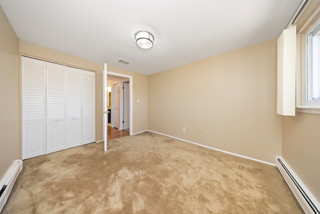 unfurnished bedroom with visible vents, a baseboard heating unit, baseboard heating, carpet flooring, and a closet