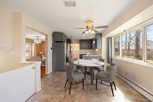 dining space featuring visible vents, stone finish flooring, baseboards, ceiling fan with notable chandelier, and a baseboard radiator