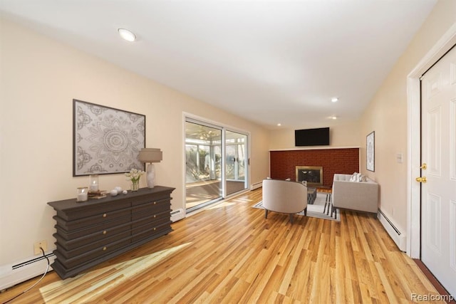 living room featuring a baseboard heating unit, a brick fireplace, and light wood-style floors