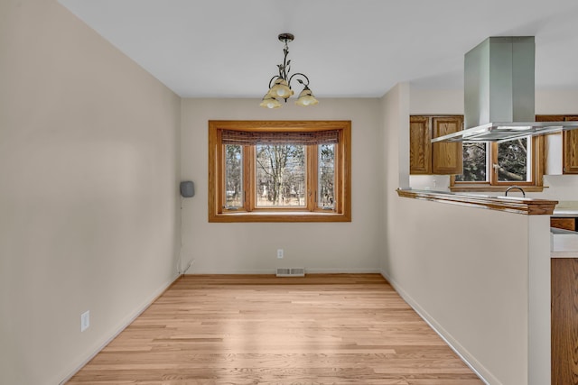 unfurnished dining area with a chandelier, light wood finished floors, visible vents, and baseboards