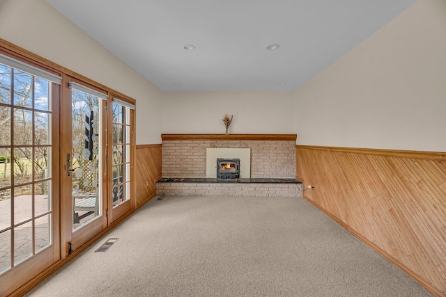 unfurnished living room featuring wooden walls, a wainscoted wall, carpet flooring, visible vents, and a wood stove