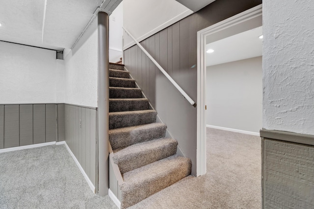 stairs with a textured wall, wainscoting, and carpet flooring