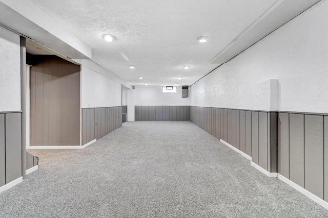 carpeted spare room featuring a textured wall, wooden walls, a textured ceiling, and wainscoting