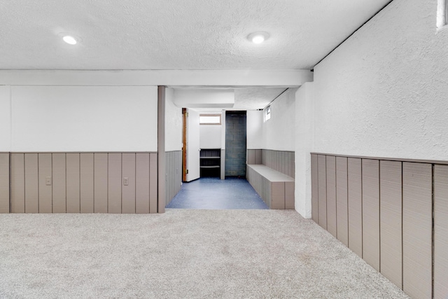 interior space featuring a textured wall, carpet, a textured ceiling, and wainscoting