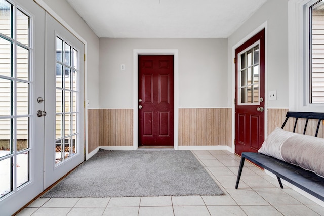 foyer entrance with light carpet, light tile patterned floors, wooden walls, wainscoting, and french doors