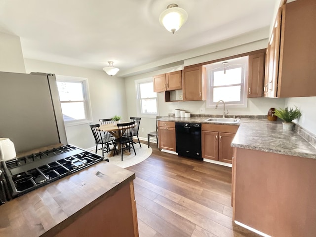 kitchen featuring black dishwasher, freestanding refrigerator, a sink, wood finished floors, and baseboards