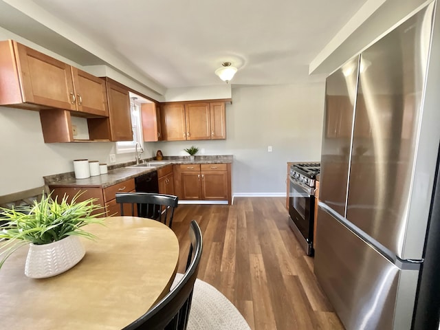 kitchen featuring baseboards, dark wood finished floors, brown cabinets, stainless steel appliances, and a sink