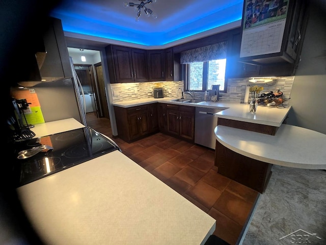 kitchen featuring a peninsula, light countertops, backsplash, dishwasher, and a raised ceiling