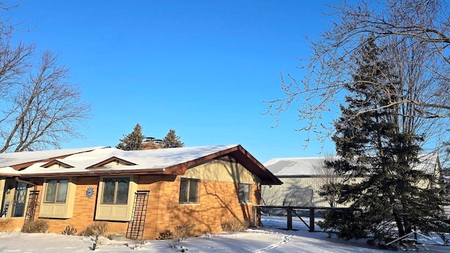 snow covered property with a gate, a chimney, and brick siding