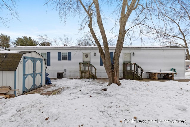 snow covered house featuring a storage unit, central AC, and an outbuilding