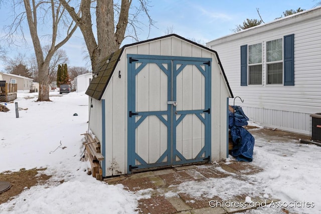 snow covered structure featuring a storage unit and an outbuilding