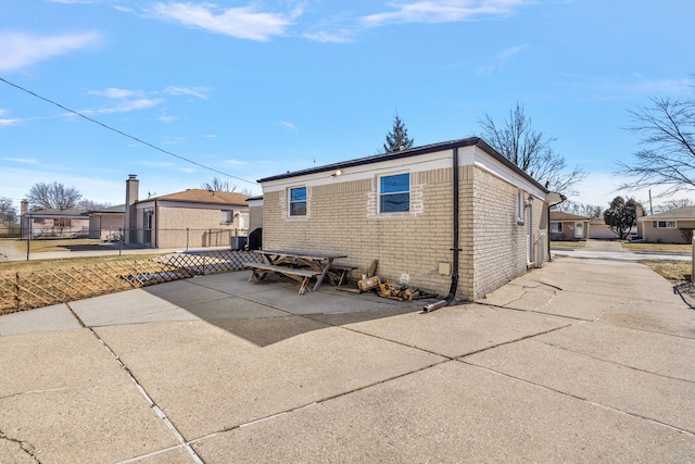 view of side of property featuring driveway, brick siding, a patio area, and fence