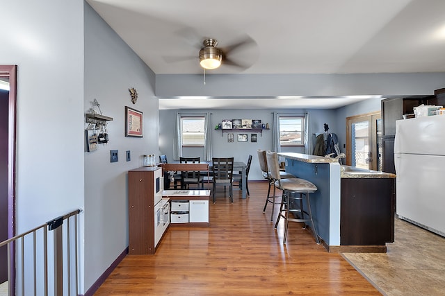 kitchen featuring baseboards, light wood-style flooring, ceiling fan, a breakfast bar area, and freestanding refrigerator