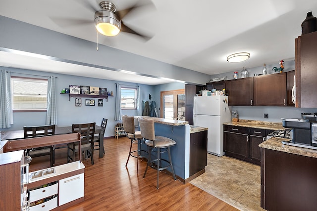 kitchen featuring a center island, light wood finished floors, freestanding refrigerator, dark brown cabinets, and a kitchen bar