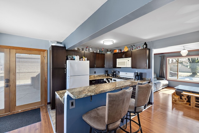 kitchen featuring white appliances, a breakfast bar area, dark brown cabinets, french doors, and light wood-style floors