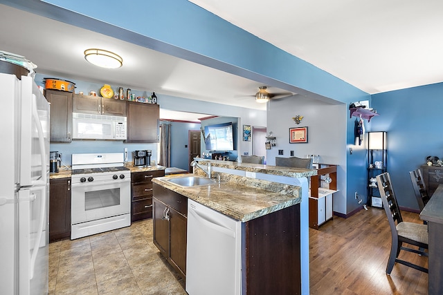 kitchen with ceiling fan, a kitchen island with sink, dark brown cabinetry, white appliances, and a sink