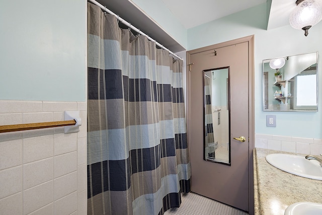 bathroom with a wainscoted wall, tile walls, double vanity, curtained shower, and a sink