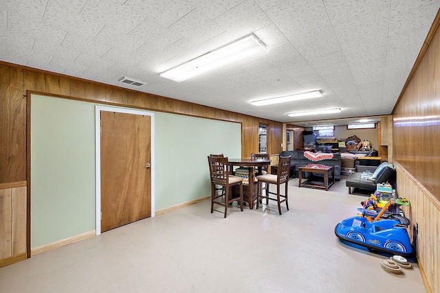 dining area with baseboards, wood walls, visible vents, and finished concrete floors