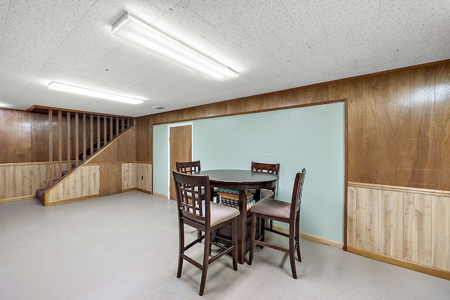 dining space with wooden walls, stairs, and finished concrete floors