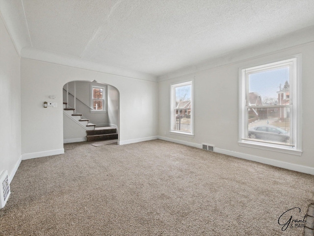 unfurnished living room featuring carpet floors, stairway, visible vents, and arched walkways