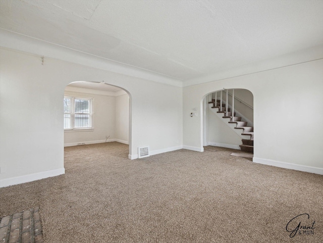 carpeted spare room with arched walkways, stairway, visible vents, and baseboards