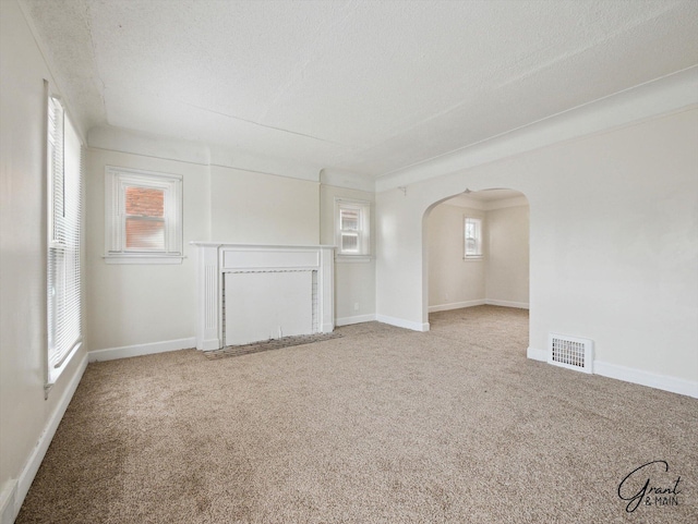 unfurnished living room featuring visible vents, arched walkways, baseboards, carpet, and a textured ceiling