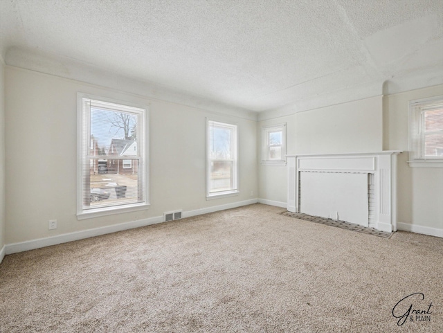 unfurnished living room featuring carpet floors, a wealth of natural light, visible vents, and a textured ceiling