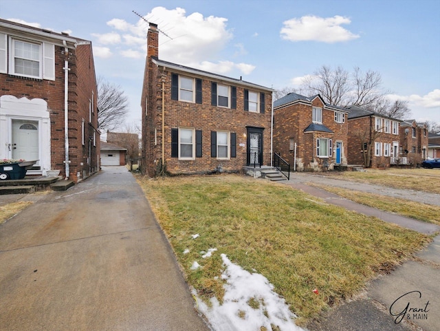 view of front of property featuring a chimney, a detached garage, an outbuilding, a front lawn, and brick siding