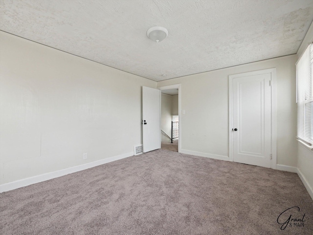 unfurnished bedroom with carpet, visible vents, a textured ceiling, and baseboards